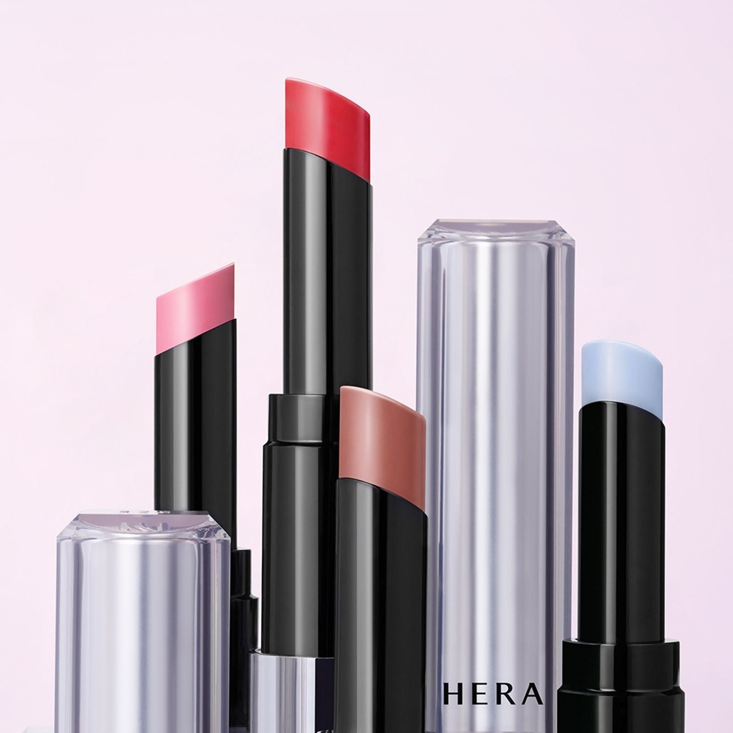 Assorted shades of HERA Sensual Nude Balm 3.5g lipsticks against a soft pink background, featuring sleek and modern packaging.