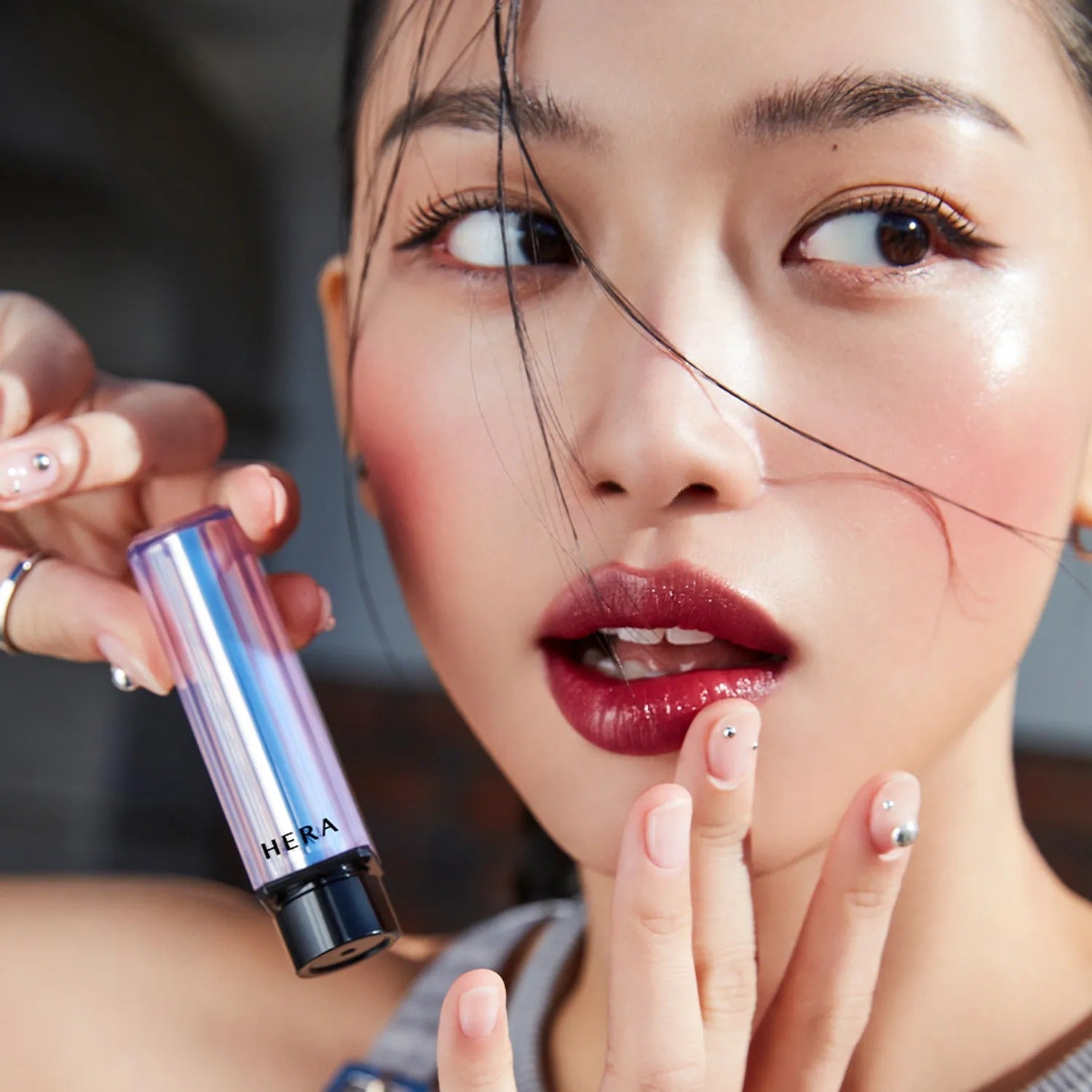 Woman applying HERA Sensual Tinted Shine Stick 3.5g, showcasing vibrant glossy lips and radiant makeup look.