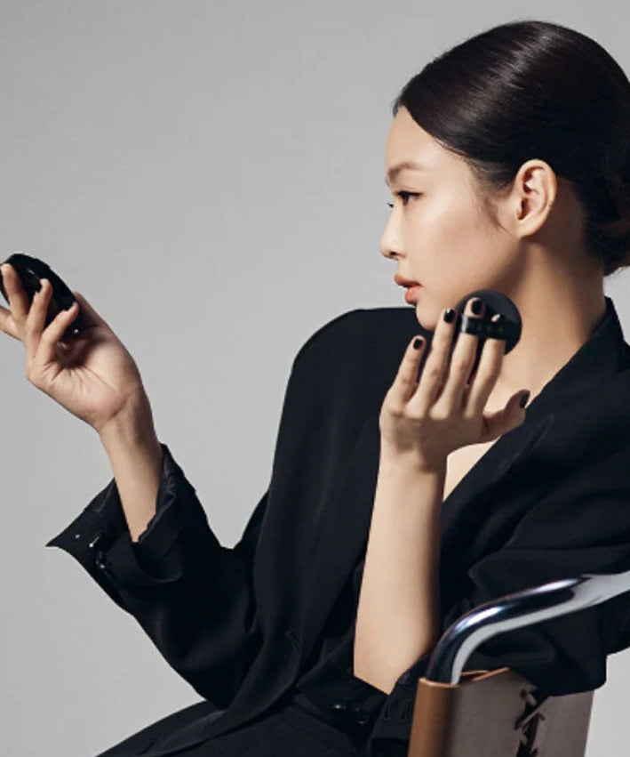 Woman applying HERA Black Cushion Foundation SPF34 PA++ 15g, showcasing sleek compact design and smooth application.