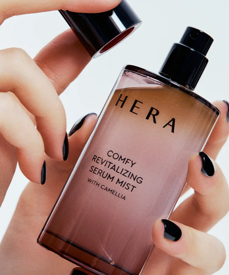 HERA Comfy Revitalizing Serum Mist 90ml bottle being held, highlighting the product's sleek design and luxurious appearance.