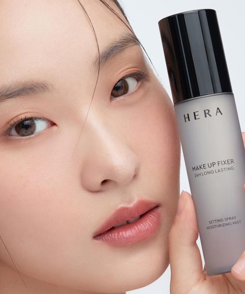 HERA Make Up Fixer 80ml setting spray held by model showcasing 24h long-lasting formula