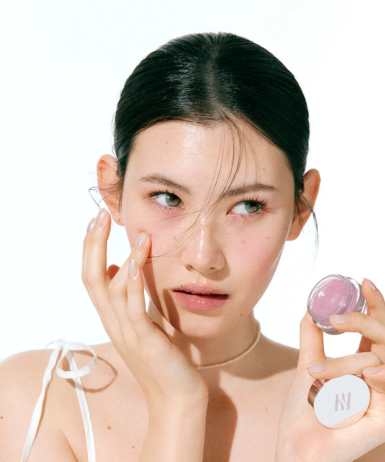 Woman applying HERA Sensual Lip & Cheek 7g to her cheeks, showcasing versatile makeup use.