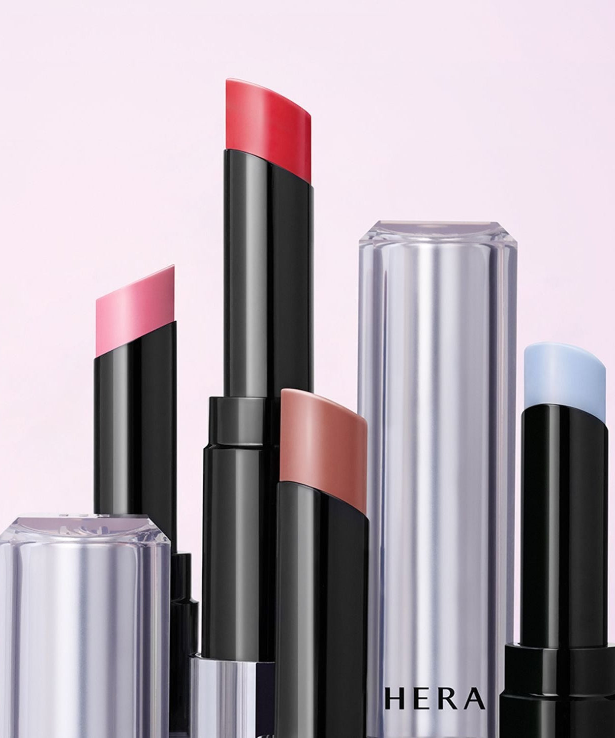 Assorted shades of HERA Sensual Nude Balm 3.5g lipsticks against a soft pink background, featuring sleek and modern packaging.