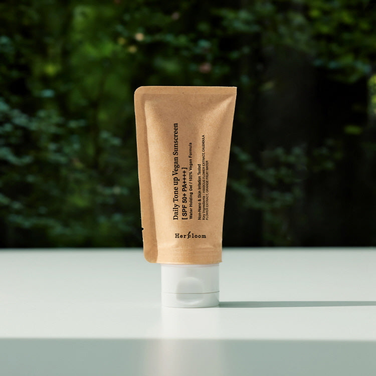 HERBLOOM Daily Tone-Up Vegan Sunscreen 50ml on a table with a forest background