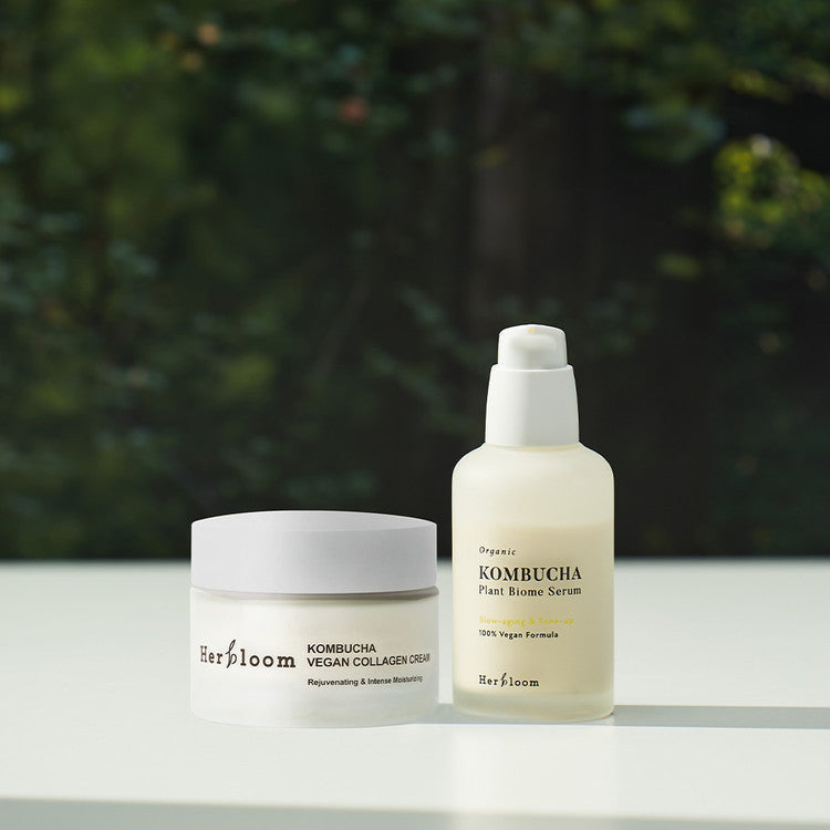 HERBLOOM Kombucha Nourishing Set (Cream+Serum) displayed on a table with lush greenery in the background.