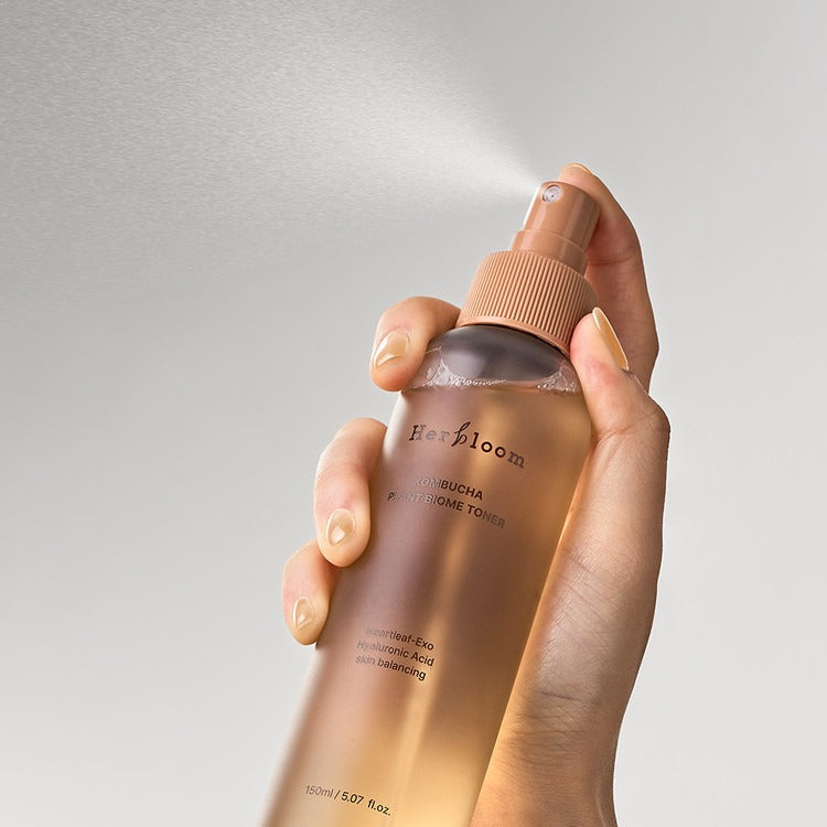 Hand holding HERBLOOM Kombucha Plant Biome Toner 150g spray bottle, showing misting action.