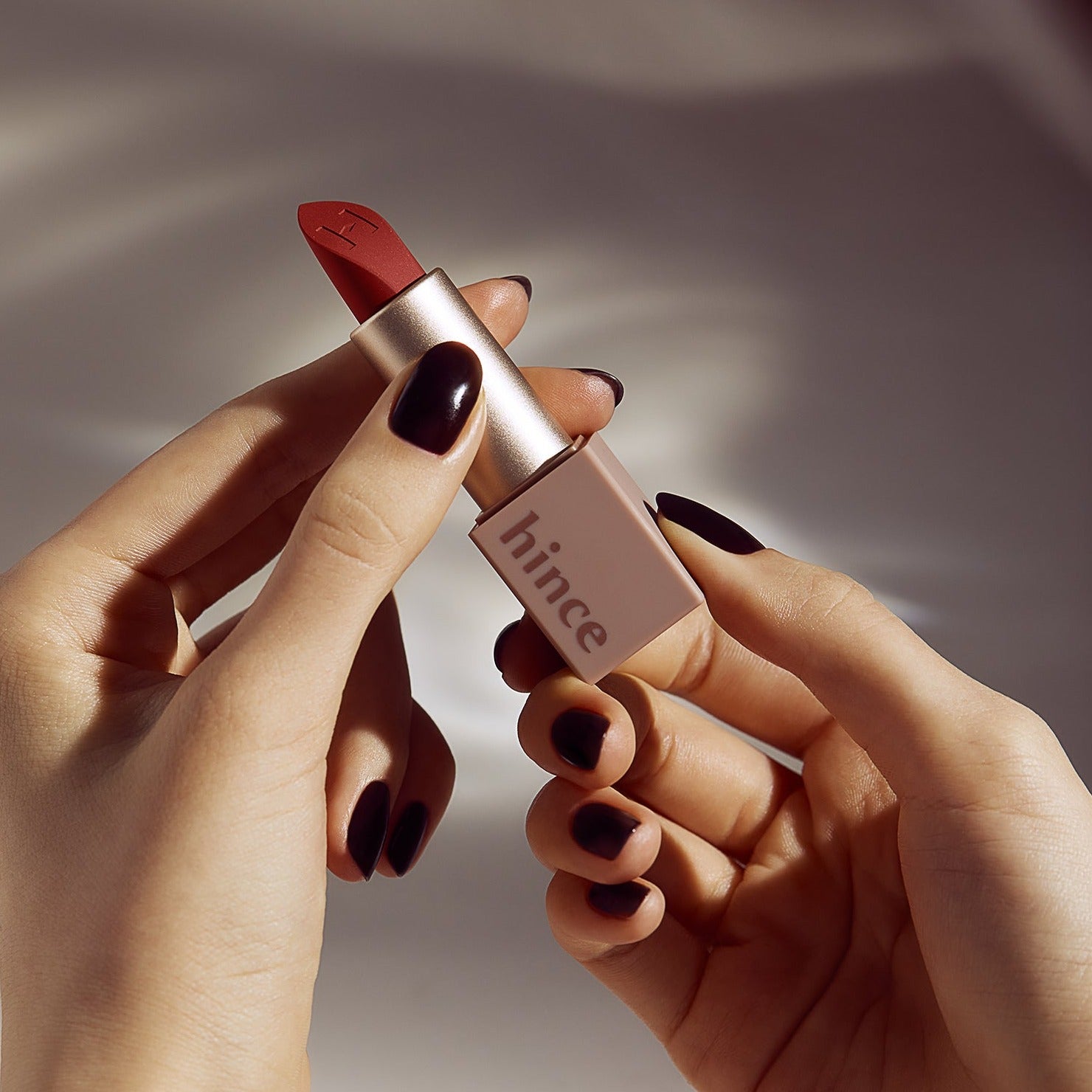 HINCE Mood Enhancer Matte lipstick held in hands with dark nail polish