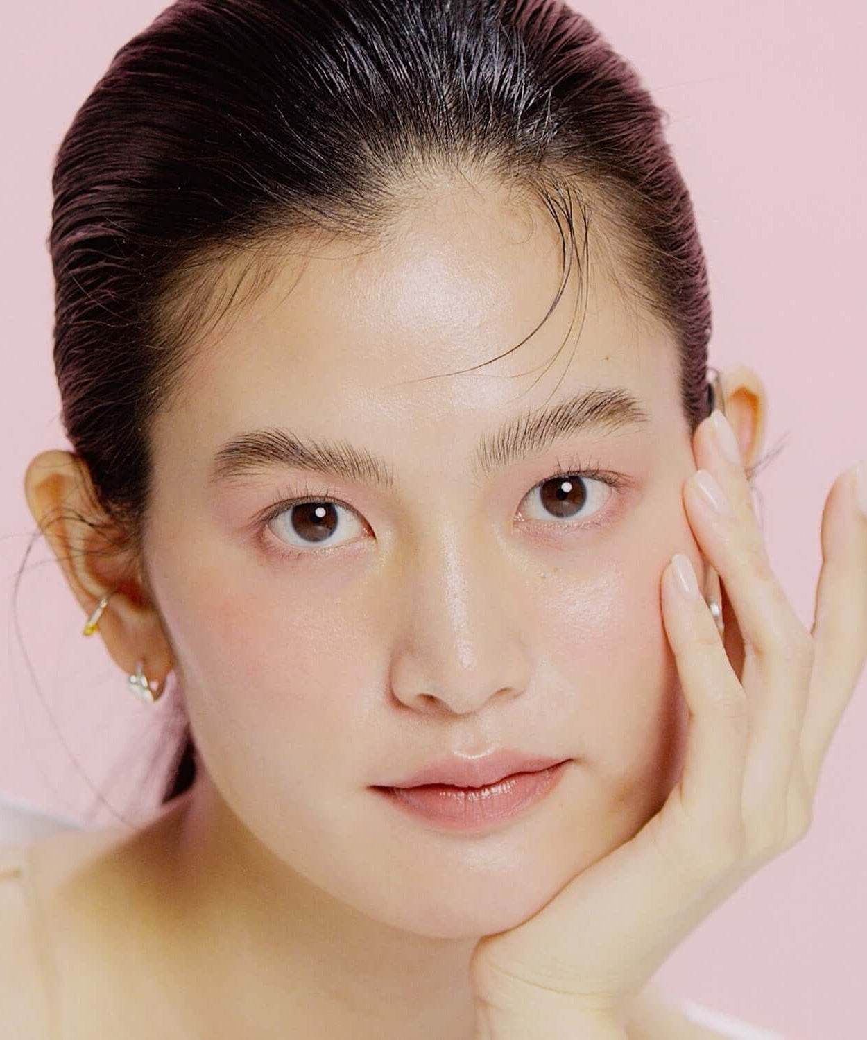 Model with smooth skin using HINCE Second Skin Hydrating Primer against a pink background, showcasing the product's moisturizing effect.