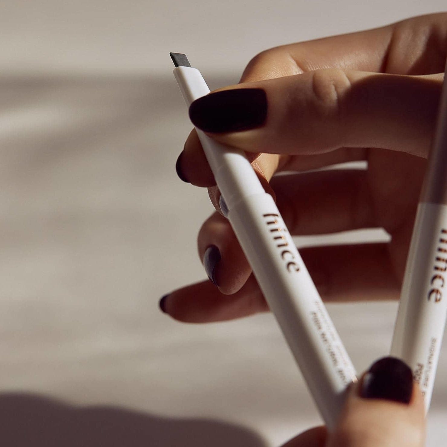 Person holding HINCE Signature Brow Pencil with black nails.