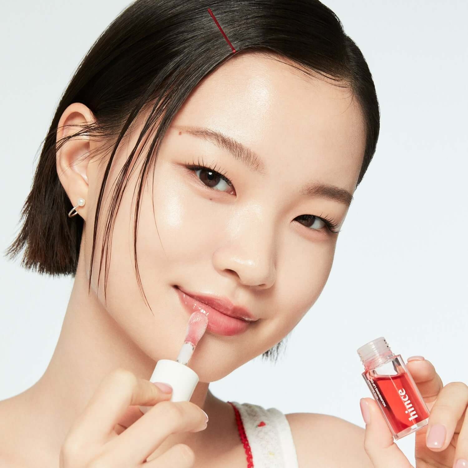 Woman applying HINCE Vita Barrier Nourishing Lip Oil from a small bottle, showcasing glossy lip care product for hydration and nourishment.