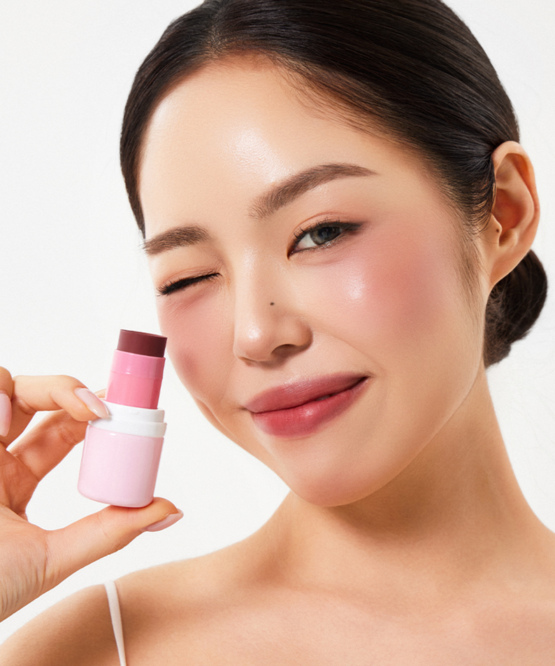 Woman holding HOUSE OF HUR Every Cheek Blush in a pink shade, smiling with soft, glowing skin.