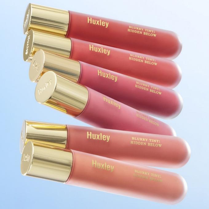 HUXLEY Blurry Tint Hidden Below lip tint collection in various shades on a blue background.
