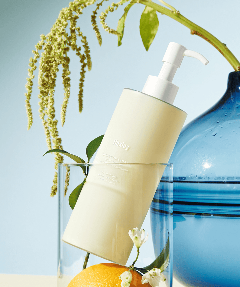 HUXLEY Body Lotion Blue Madina Tangerine bottle with pump on display with decorative elements in the background