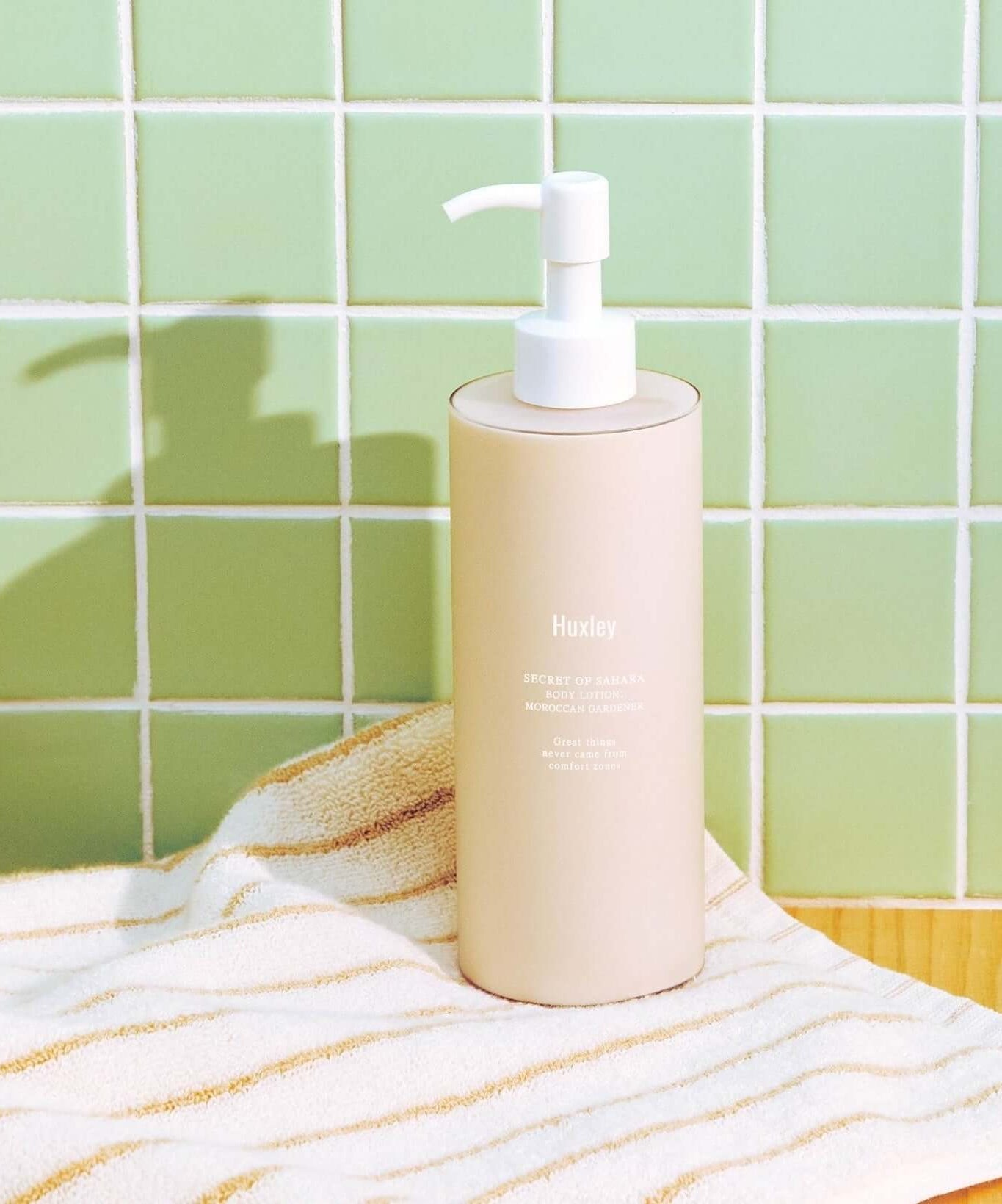 HUXLEY Body Lotion Blue Madina Tangerine bottle on a bathroom counter next to a striped towel.