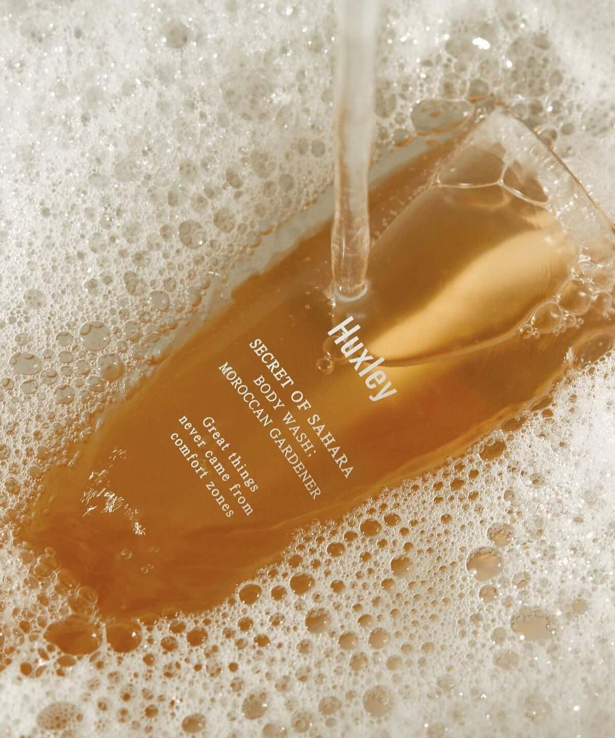 HUXLEY Body Wash Blue Medina Tangerine in foamy bath setting, showcasing luxurious bottle design and branding in use.