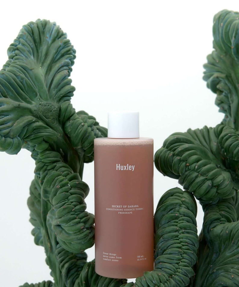 HUXLEY Conditioning Essence Toner Preshape bottle surrounded by green plants, showcasing natural beauty and skincare benefits.
