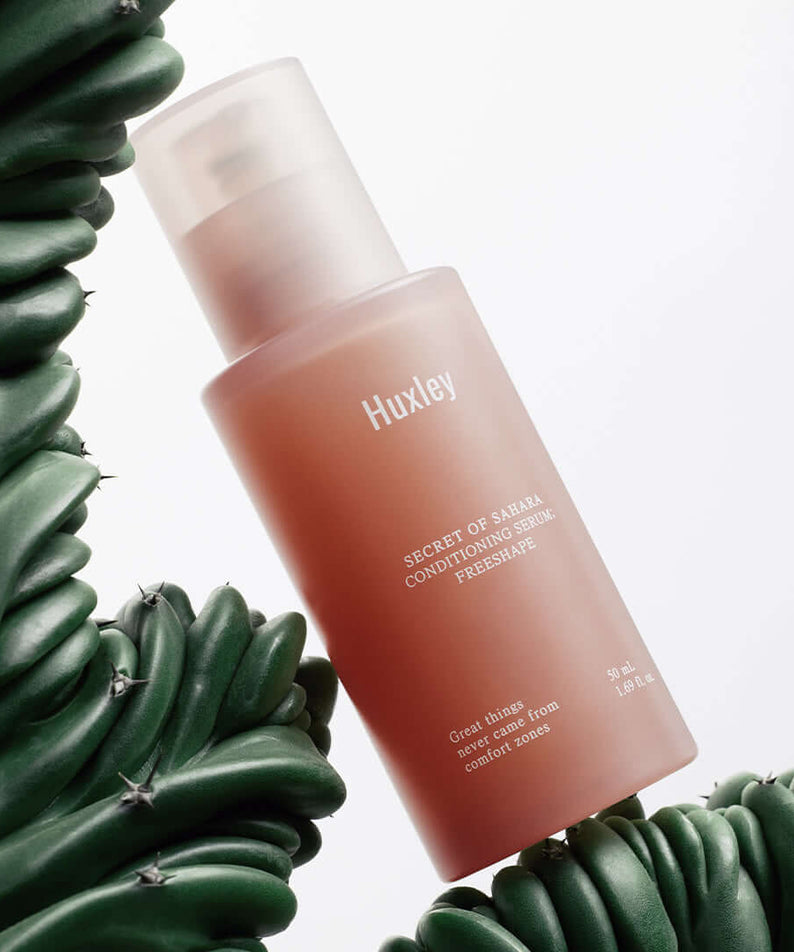 HUXLEY Conditioning Serum Preshape bottle surrounded by green cactus plant, enhancing skincare and hydration benefits.