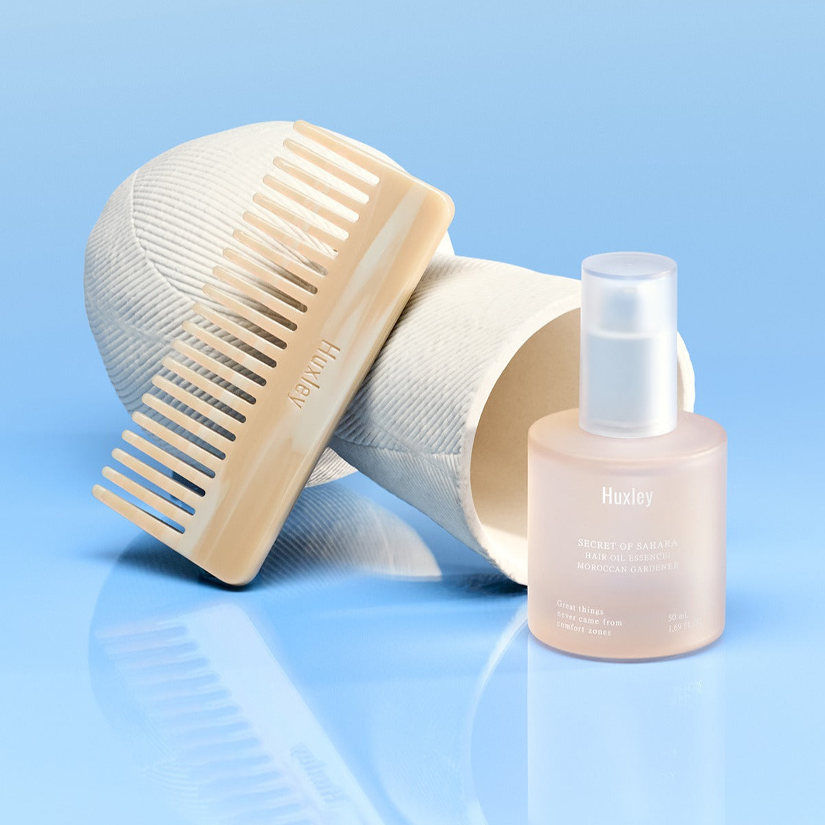 HUXLEY Hair Oil Essence Moroccan Gardener 50ml with comb, perfect for nourishing and styling hair, on a blue background.