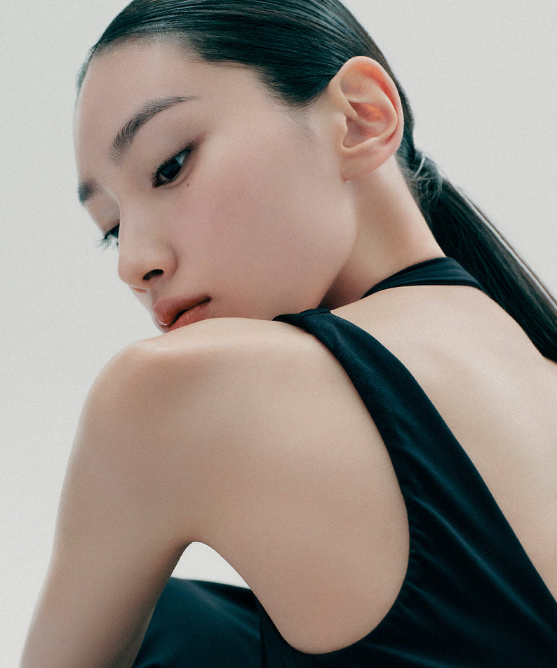 Profile of a woman with sleek dark hair and a black sleeveless top facing away, showcasing her smooth and flawless skin.