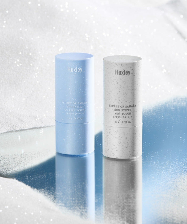 HUXLEY Sun Stick Watery Touch 20g on reflective surface with snow-like background.