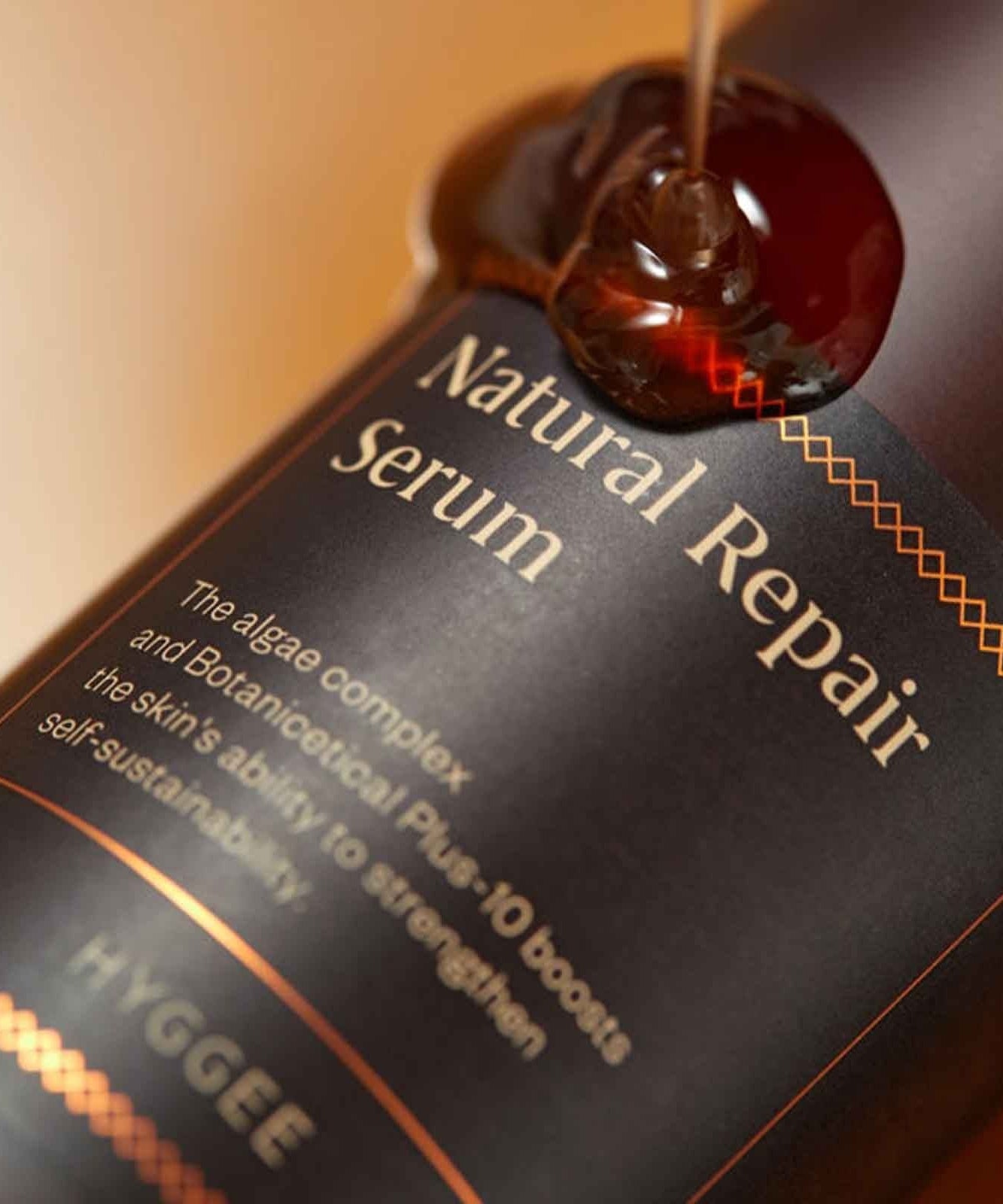 Close-up of HYGGEE Natural Repair Serum 120ml bottle with liquid serum dripping for skincare.
