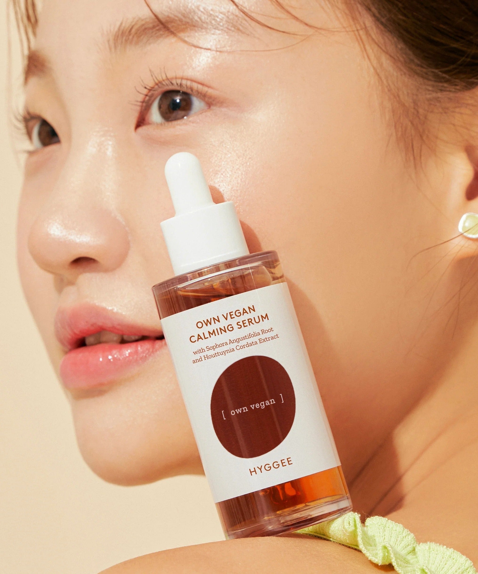 Close-up of a model holding HYGGEE Own Vegan Calming Serum 50ml with glowing skin.