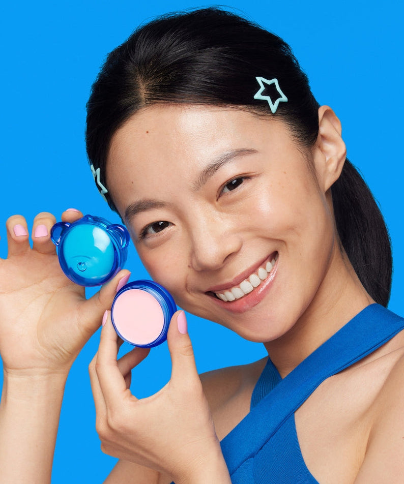 Person holding DR.JART+ Vital Hydra Solutionâ„¢ Hydrating Lip Mask with a smile on a blue background.