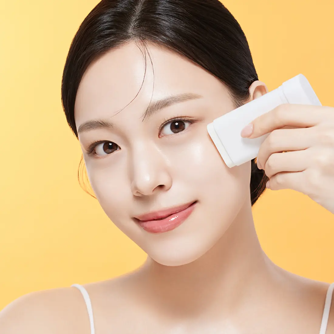 Woman applying ILLIYOON Daily Weaponless Sun Stick 20g on face with yellow background.
