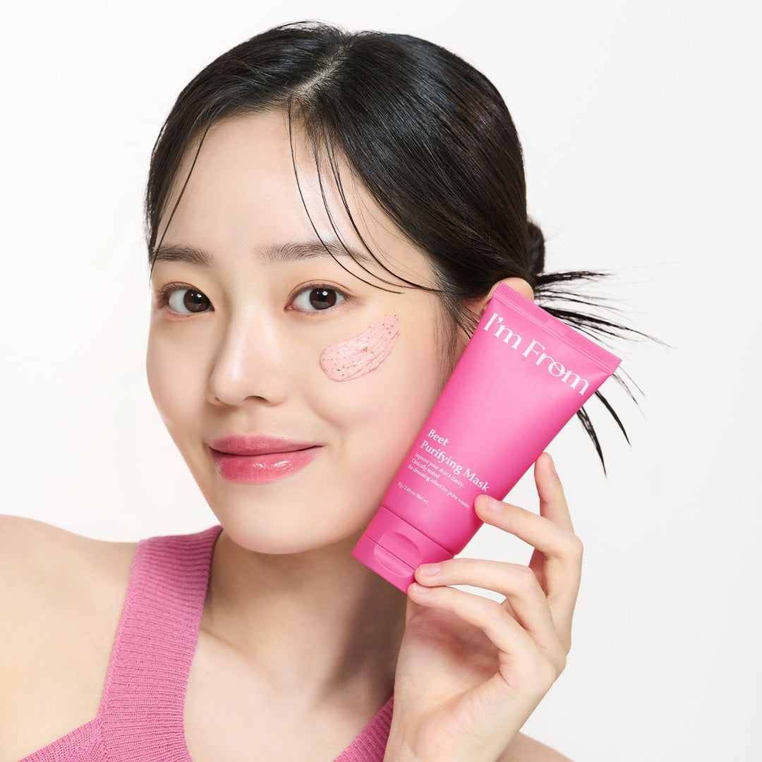 Woman holding I'M FROM Beet Purifying Mask 70g with product applied on cheek, showcasing skincare use.