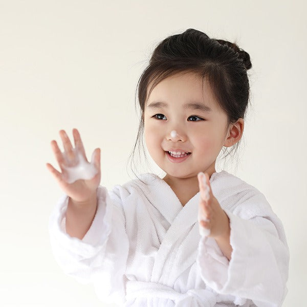 Child smiling using I'M NOT BABY Kids Facial Cleanser 150ml, wearing a white bathrobe, demonstrating skincare routine