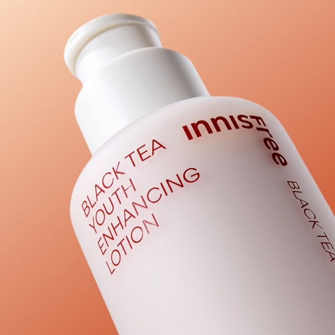 Bottle of INNISFREE Black Tea Youth Enhancing Lotion 170ml against an orange background