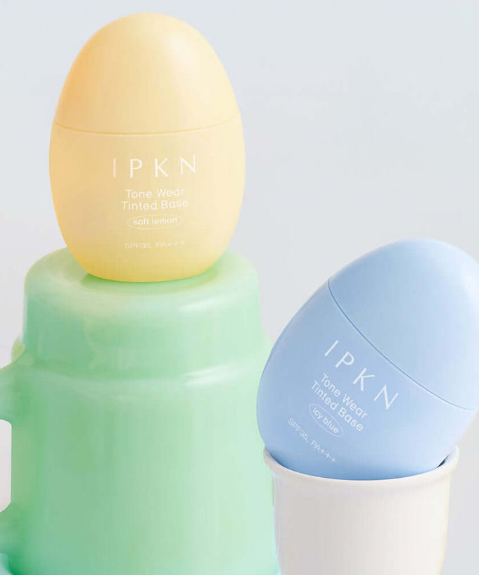 IPKN Tone Wear Tinted Base in soft yellow and blue, enhancing skin tone and texture, displayed in an elegant setting.