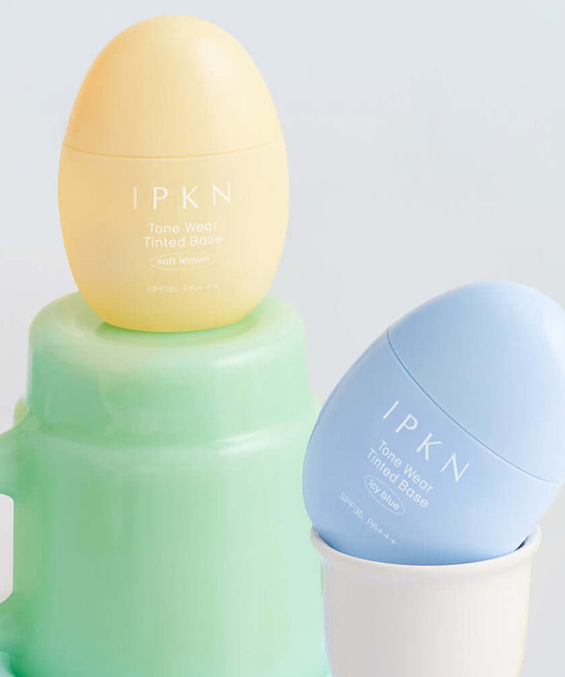 IPKN Tone Wear Tinted Base in soft yellow and blue, enhancing skin tone and texture, displayed in an elegant setting.