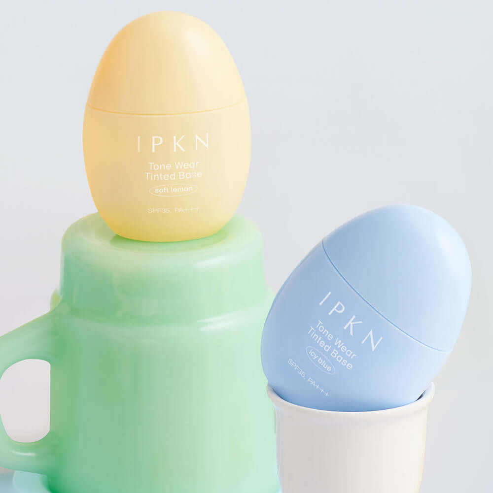 IPKN Tone Wear Tinted Base in soft yellow and blue, enhancing skin tone and texture, displayed in an elegant setting.
