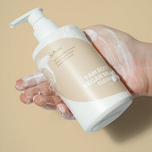 Hand holding a bottle of ISNTREE Yam Root Vegan Milk Cleanser 220ml with creamy texture, emphasizing gentle skincare solution.