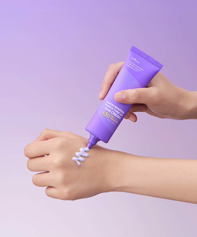 Hand applying ISNTREE Onion Newpair Purple Tone-Up Sunscreen 50ml cream on wrist against a purple background