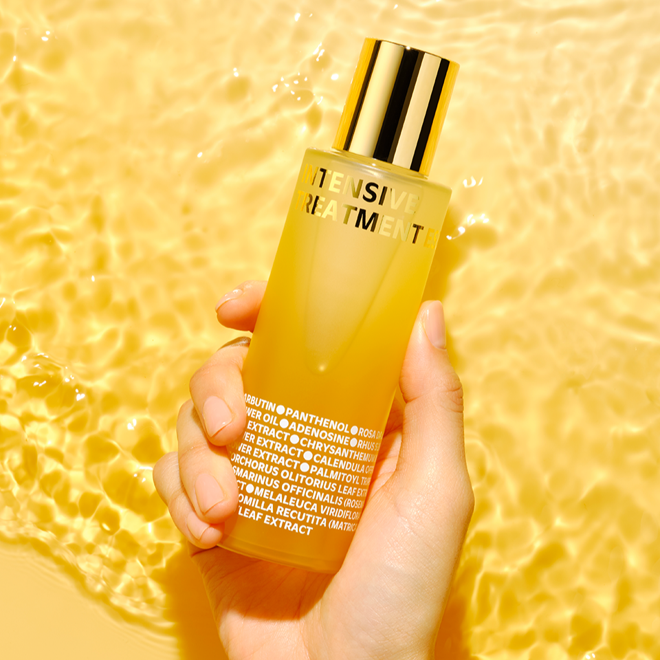 Hand holding ISOI Intensive Treatment Essence 130ml bottle against a golden background.