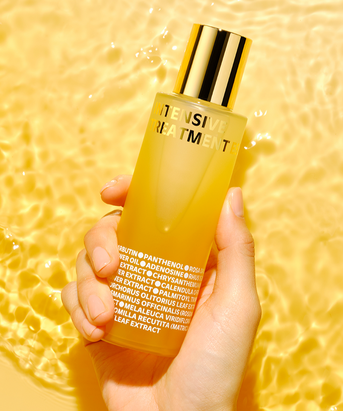 Hand holding ISOI Intensive Treatment Essence 130ml bottle against a golden background.