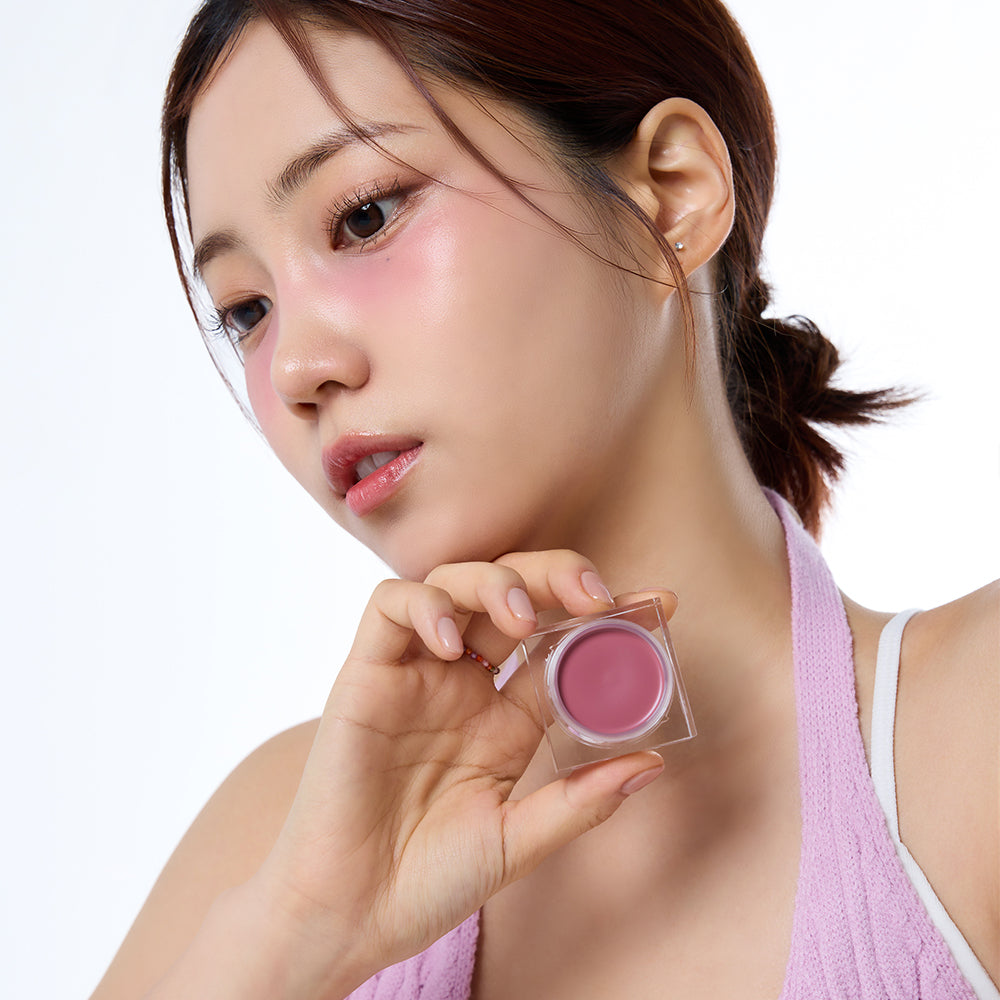 Person posing with IVI MAD PEACH Mood Mix Cream Blusher applied on cheeks, holding the product in hand.
