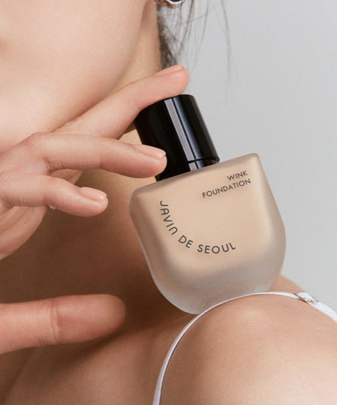 Close-up of woman holding JAVIN DE SEOUL Wink Foundation 30g bottle with elegant design.