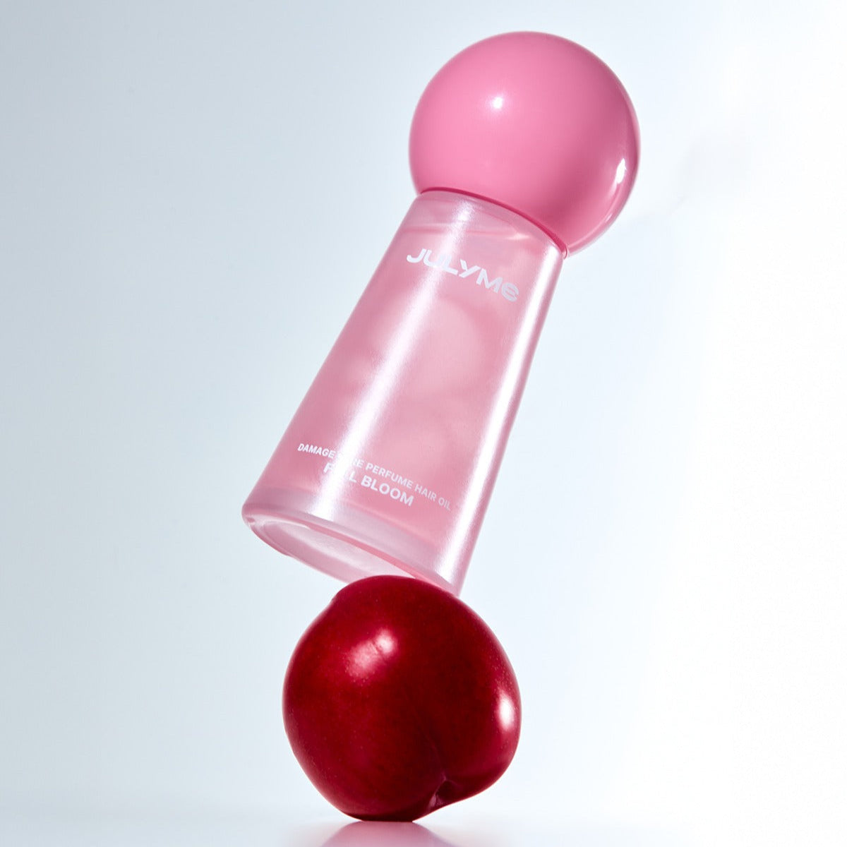JULYME Damage Care Perfume Hair Oil 30ml in sleek pink bottle balancing on a red plum