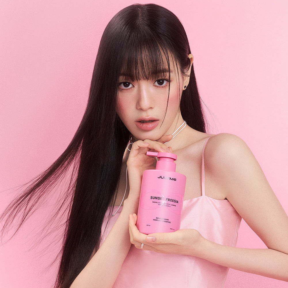 Woman holding JULYME Damage Care Collagen Shampoo 500ml (Sunset Freesia) bottle against pink background.
