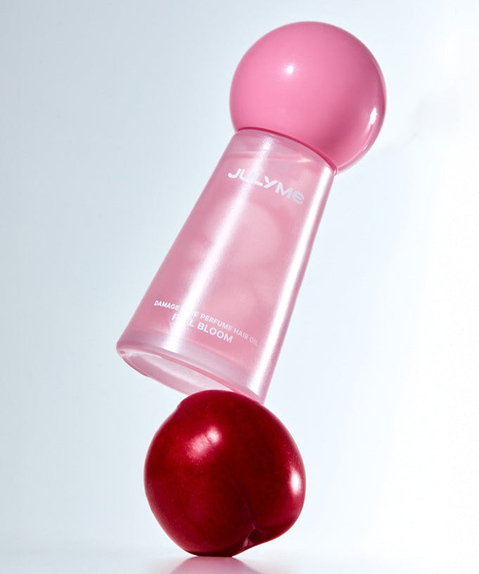 JULYME Damage Care Perfume Hair Oil 30ml in sleek pink bottle balancing on a red plum
