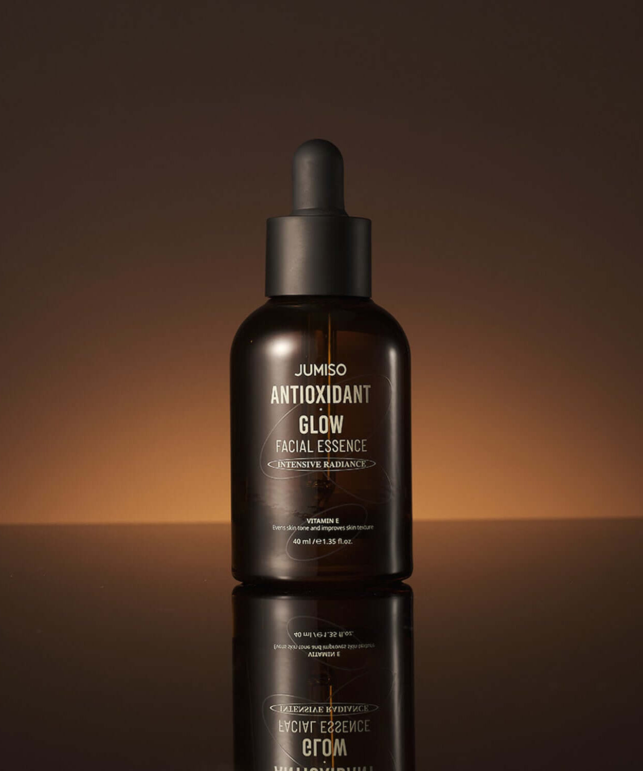 JUMISO Antioxidant Glow Facial Essence bottle on a reflective surface with a warm background