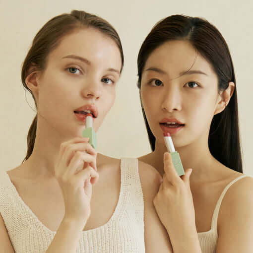 Two women applying KAINE Glow Melting Lip Balm shown in natural light.