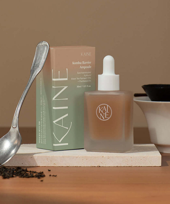 KAINE Kombu Barrier Ampoule with box on wooden table beside tea leaves and spoon