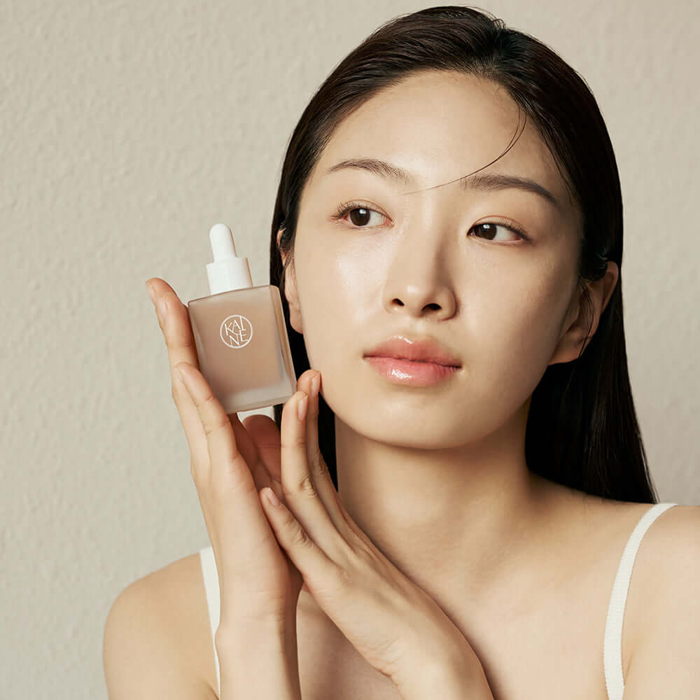 Woman holding KAINE Kombu Barrier Ampoule close to her face, showcasing skincare product and packaging.