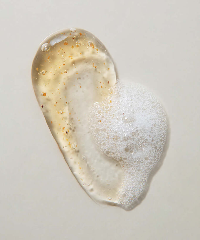 Texture of KAINE Kombu Hydrating Daily Cleanser 155g with foam and exfoliating particles on a light background.