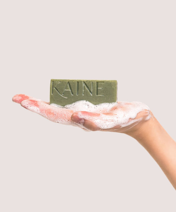 Hand holding KAINE Rosemary Acne Mildly Acidic Cleansing Bar 100g with soap suds