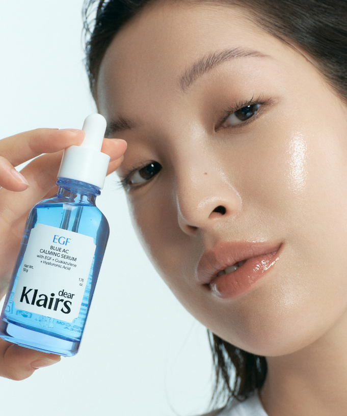 Woman holding KLAIRS EGF Blue AC Soothing Serum 50g bottle with glowing skin